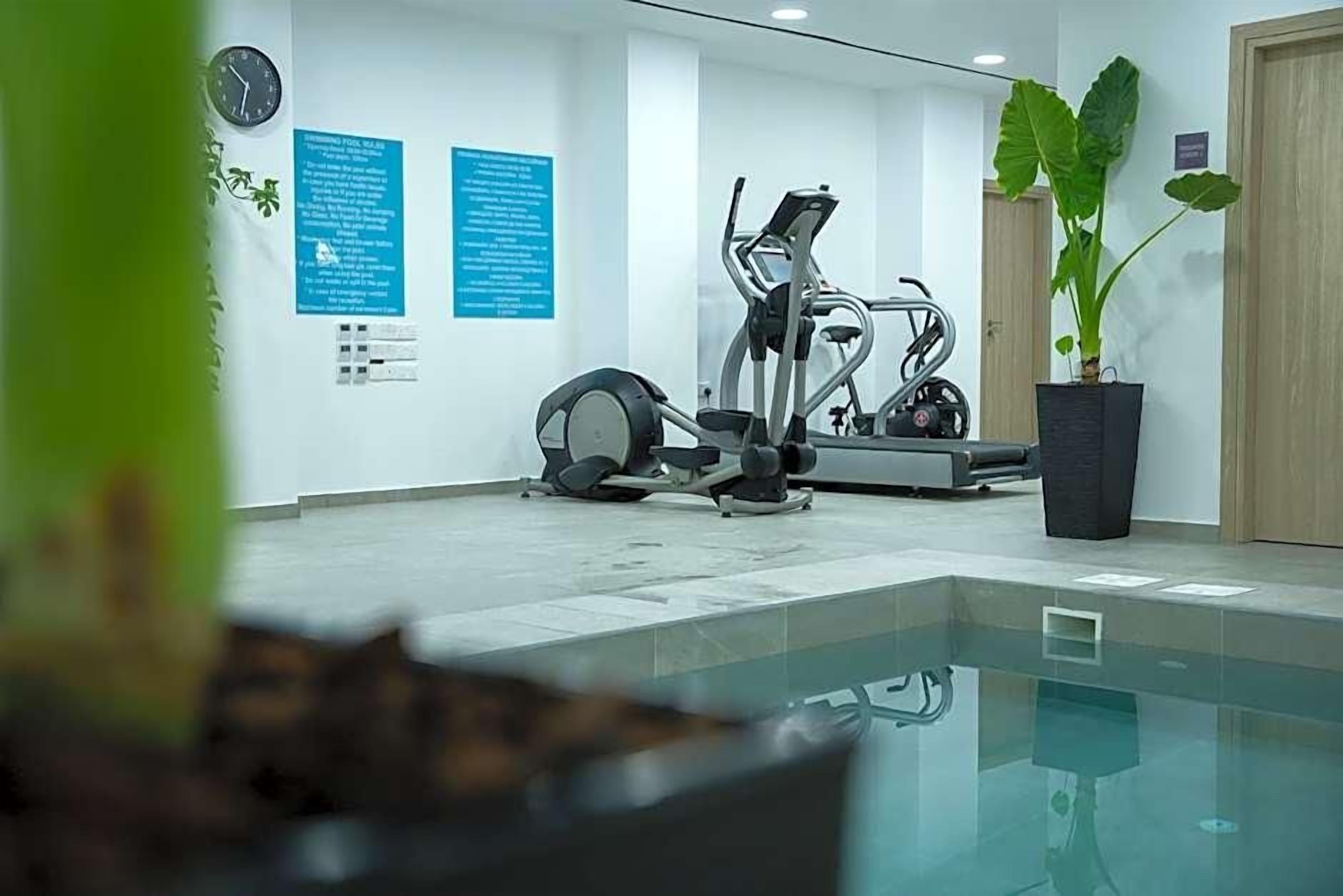 Un gimnasio moderno con equipo de ejercicio, un reloj y carteles informativos en las paredes.