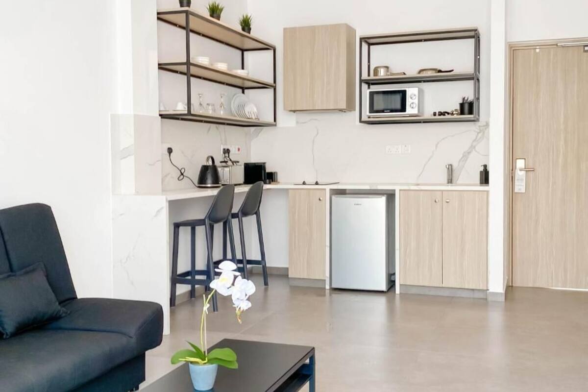 A modern kitchen with built-in appliances, a dining area with a black sofa and chairs, and a small table with a potted plant.
