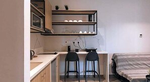 Ein kleines Schlafzimmer mit Bett, Schreibtisch, zwei Stühlen und einem Regal über dem Schreibtisch.