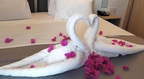 A bed with a white bedspread and pillows, a bedside table with a phone, and pink flower petals scattered on the bed. - Caramela Luxury Apartments (Ayia Napa)
