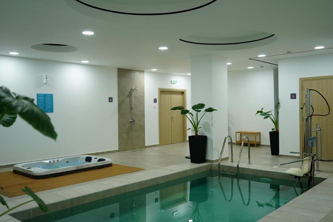 Une piscine intérieure dotée d’un jacuzzi, d’un espace douche et de plantes en pot.