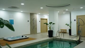 Una piscina interior con jacuzzi, zona de duchas y plantas en macetas.