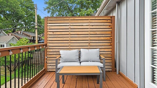 Une terrasse en bois avec un canapé et une table, une rambarde en métal et une vue sur les maisons au loin.