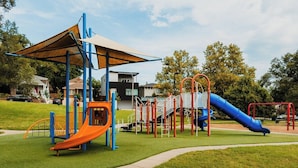Une aire de jeux avec un toboggan, des structures d’escalade et un espace ombragé.