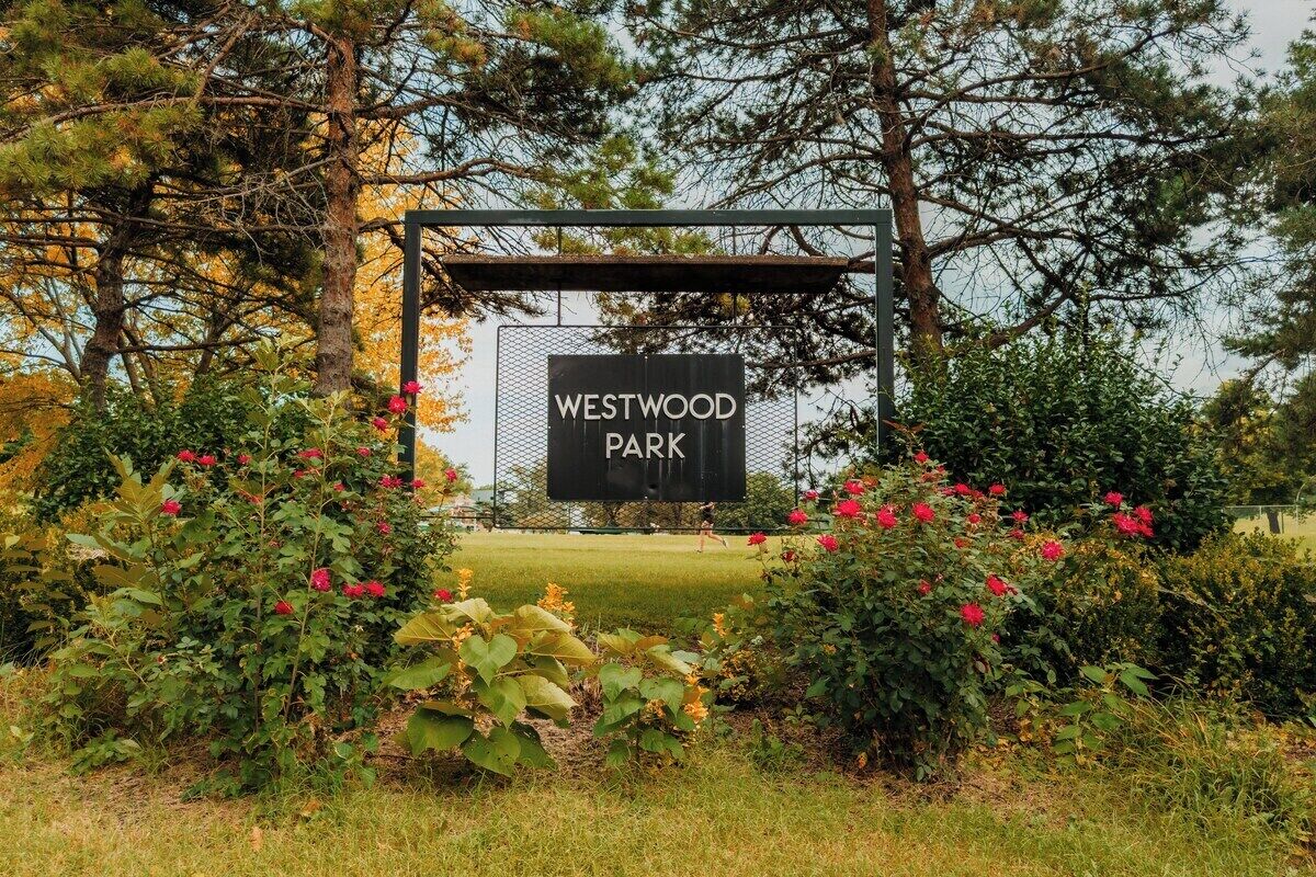 A sign for Westwood Park surrounded by lush greenery and flowering plants.