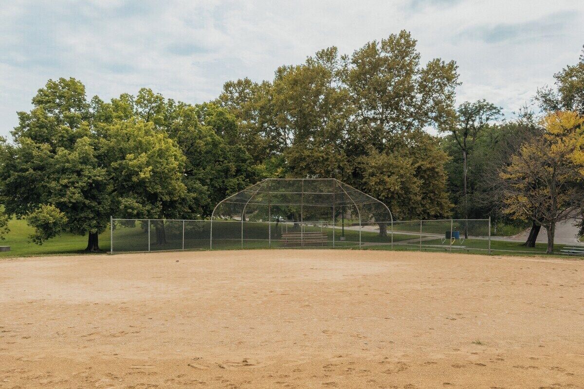 Un terrain de baseball sous un ciel dégagé, entouré d’arbres et d’une clôture.