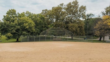 A baseball field with a clear sky, surrounded by trees and a fence.