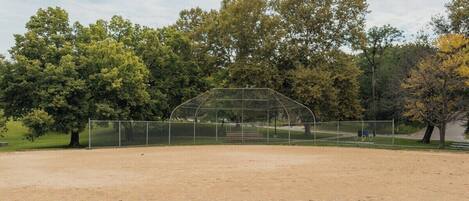 A baseball field with a clear sky, surrounded by trees and a fence.