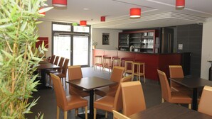 Un restaurante moderno con mesas de madera, sillas color naranja, una barra roja y un expositor de vidrio.