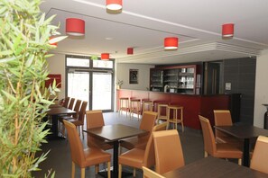 Un restaurant moderne avec des tables en bois et des chaises orange, un comptoir rouge et une vitrine.
