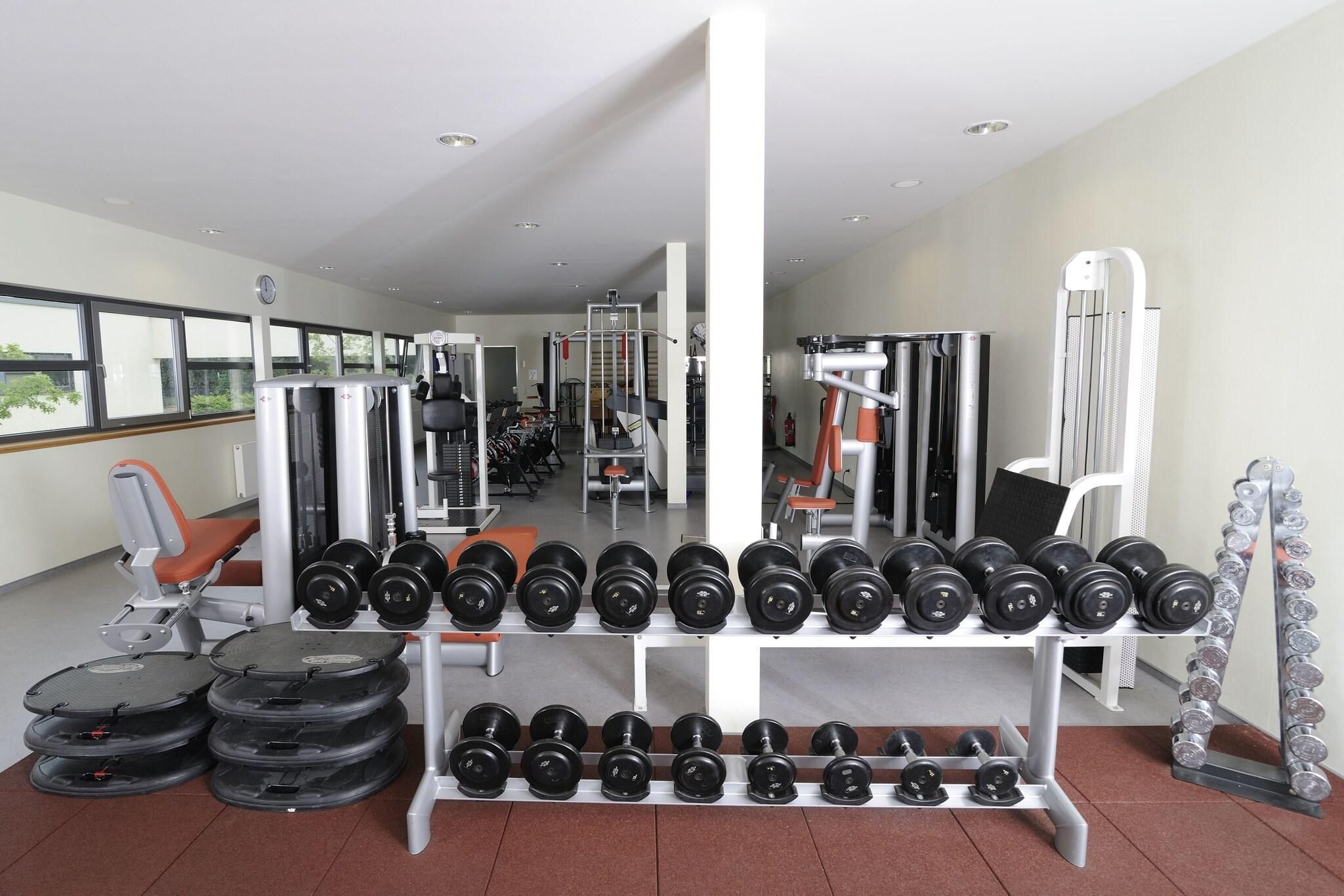 Une salle de sport équipée de divers appareils d’entraînement, notamment des haltères, des disques de poids et un banc.