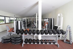 Uma academia com diversos equipamentos de ginástica, incluindo halteres, anilhas e um banco.