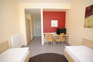 Habitación de hotel con dos camas, un escritorio con computadora, una silla y una pared de acento roja.