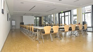 Un salón de conferencias con mesas largas y sillas, ventanas amplias y una pizarra.