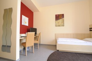 Habitación de hotel con cama, escritorio con computadora, silla y un cuadro en la pared.