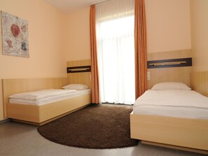 Habitación de hotel con dos camas individuales, un tapete marrón, una ventana con cortinas y un cuadro en la pared.