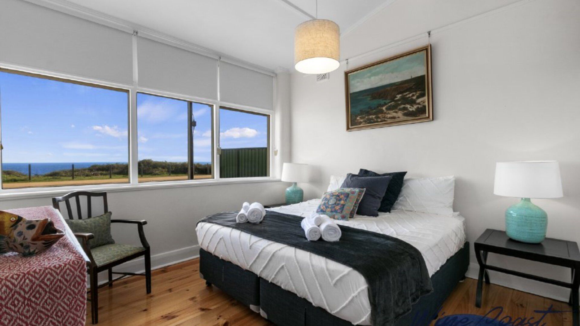 Una camera da letto con un'ampia finestra, un letto, due comodini con lampade, una sedia e un quadro appeso al muro.