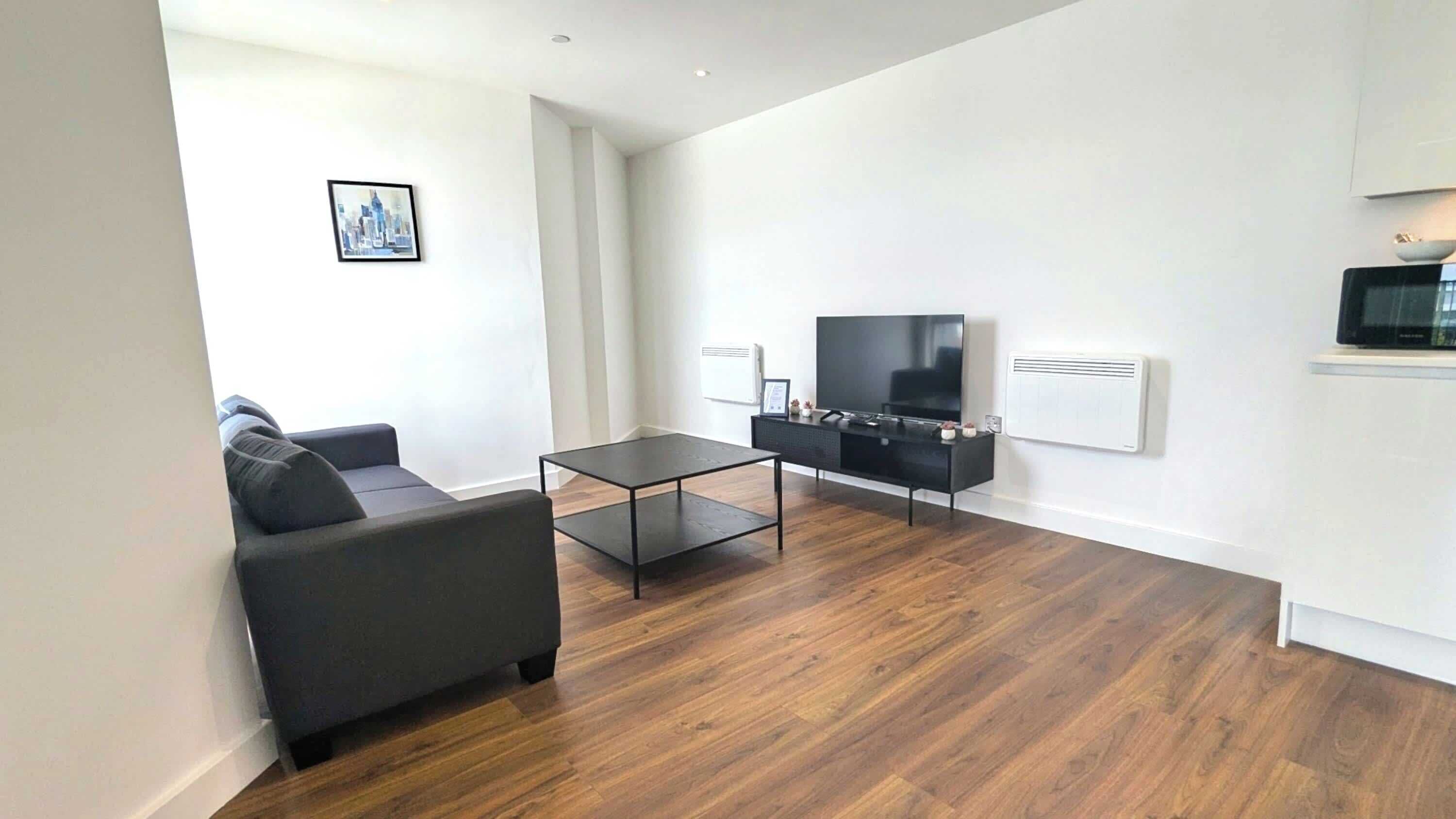 A modern living room with a black sofa, a glass coffee table, and a flat-screen TV on a black stand.