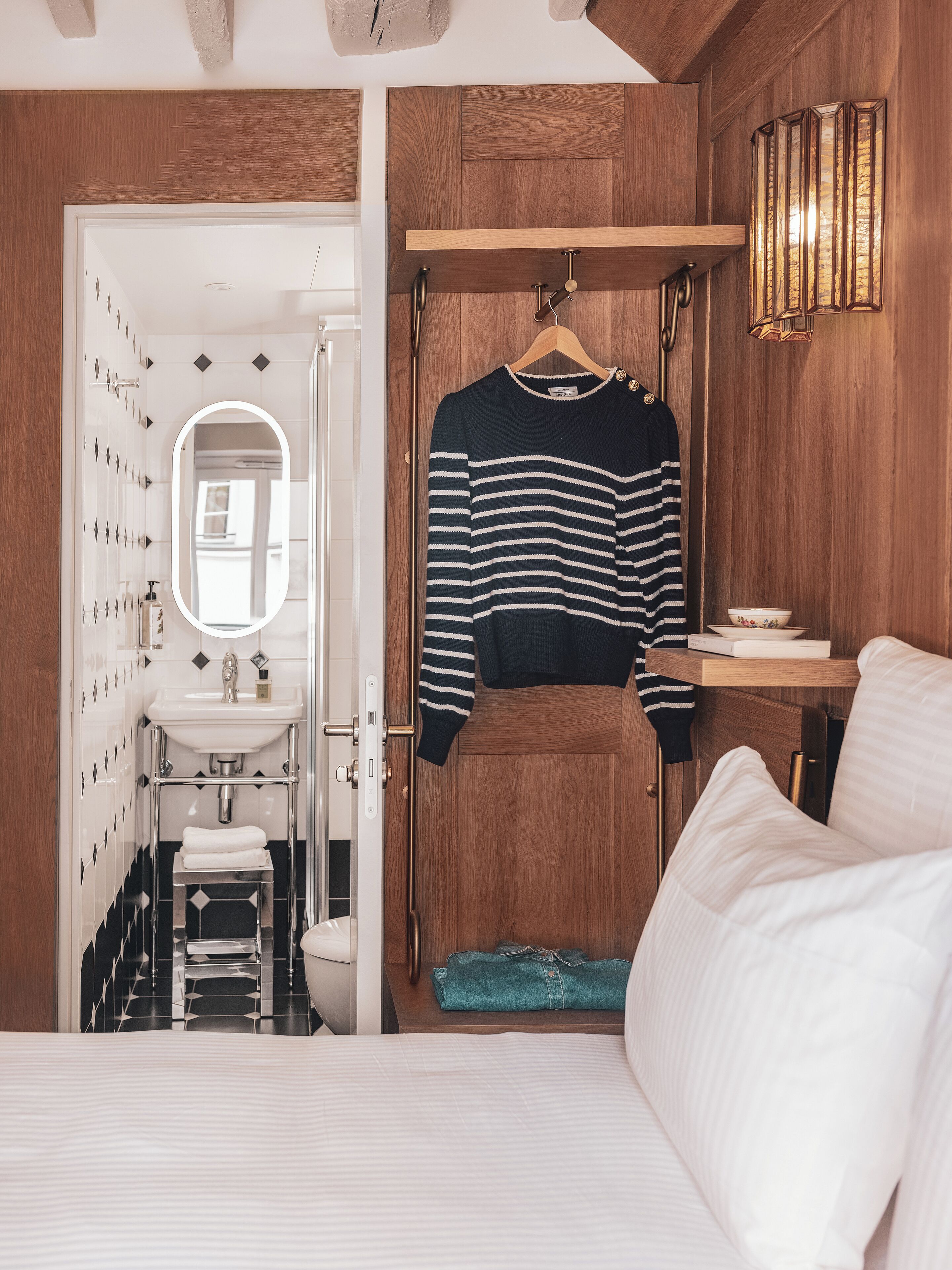 A bedroom with a bed, a bedside table, a hanging towel rack, and a wooden wardrobe.