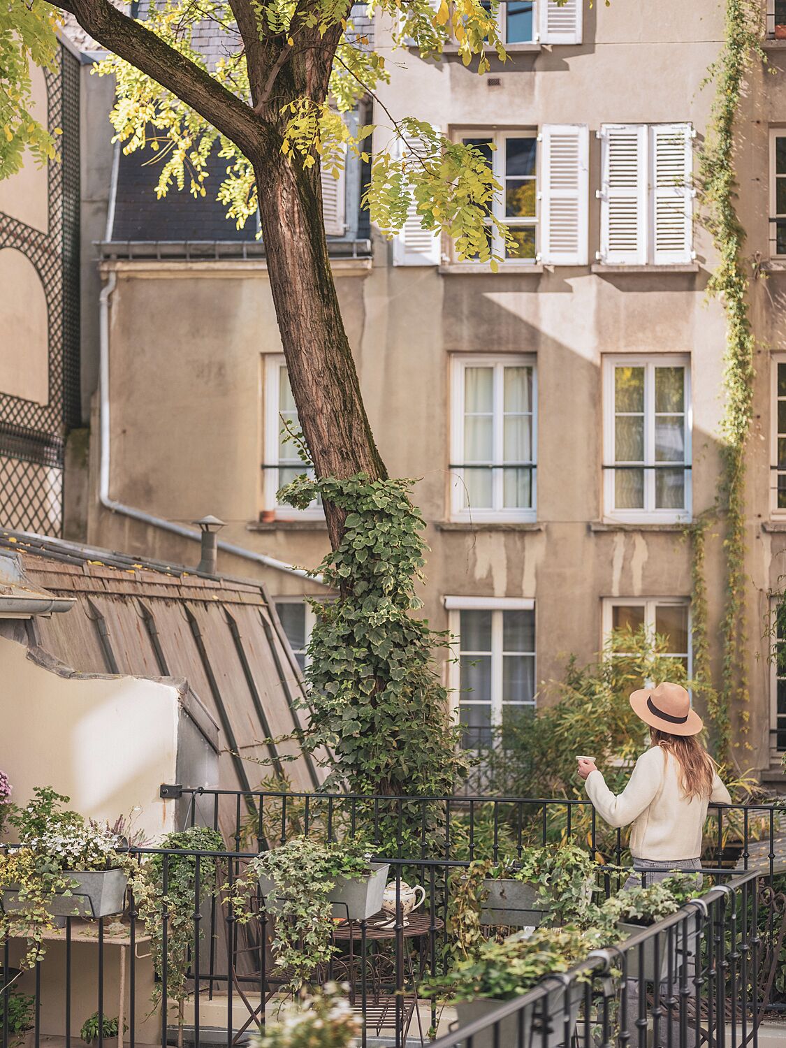Un balcone con un albero, una persona con un cappello e un edificio con finestre e persiane.
