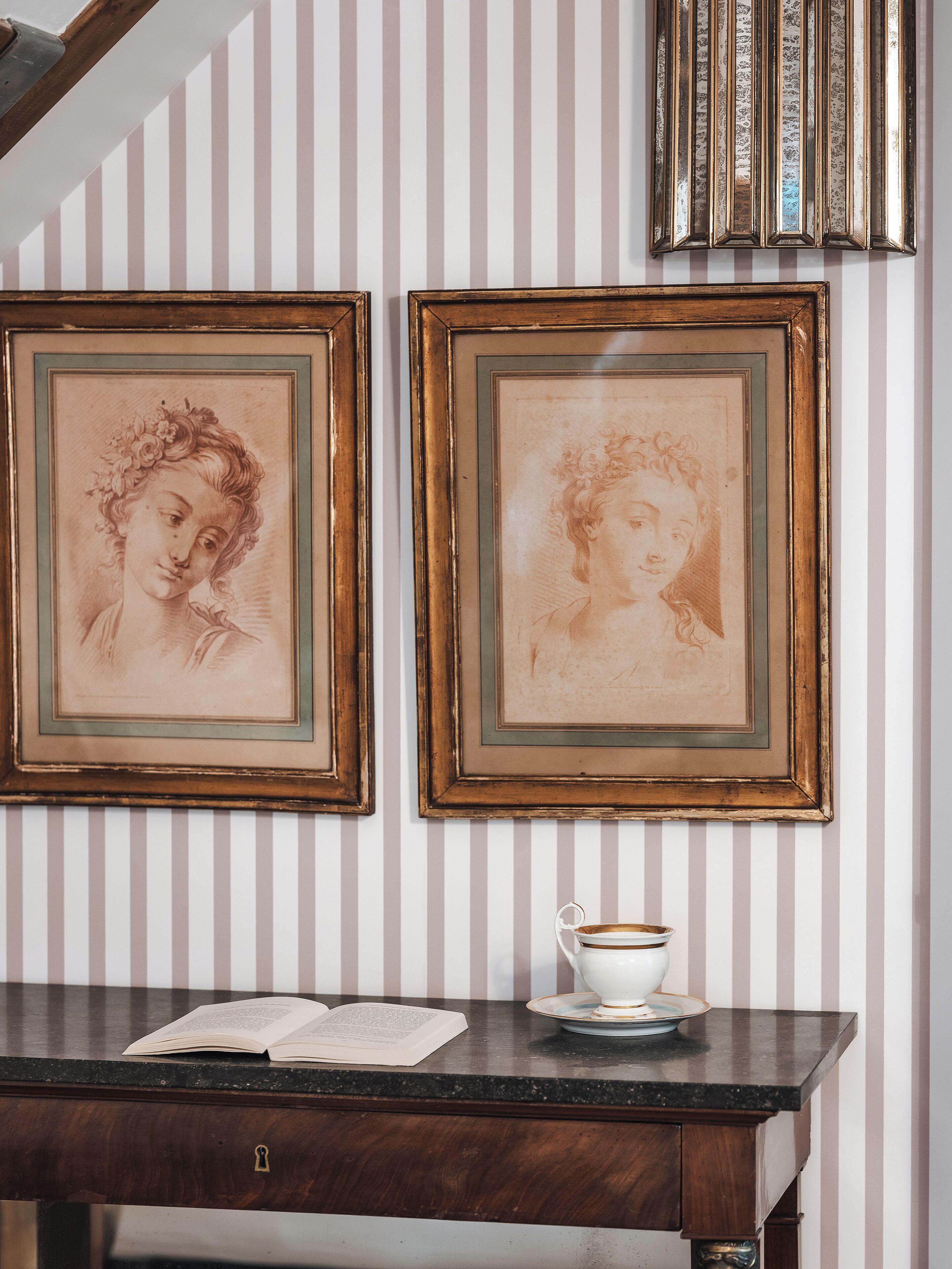 A room with a wooden desk, two framed artworks, and a striped wall.