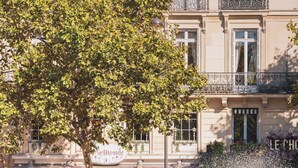 A fountain with a statue in the center, surrounded by a blue fence. In the background, there is a building with a cafe and outdoor seating. - Hotel Madeleine de Senlis (Paris)