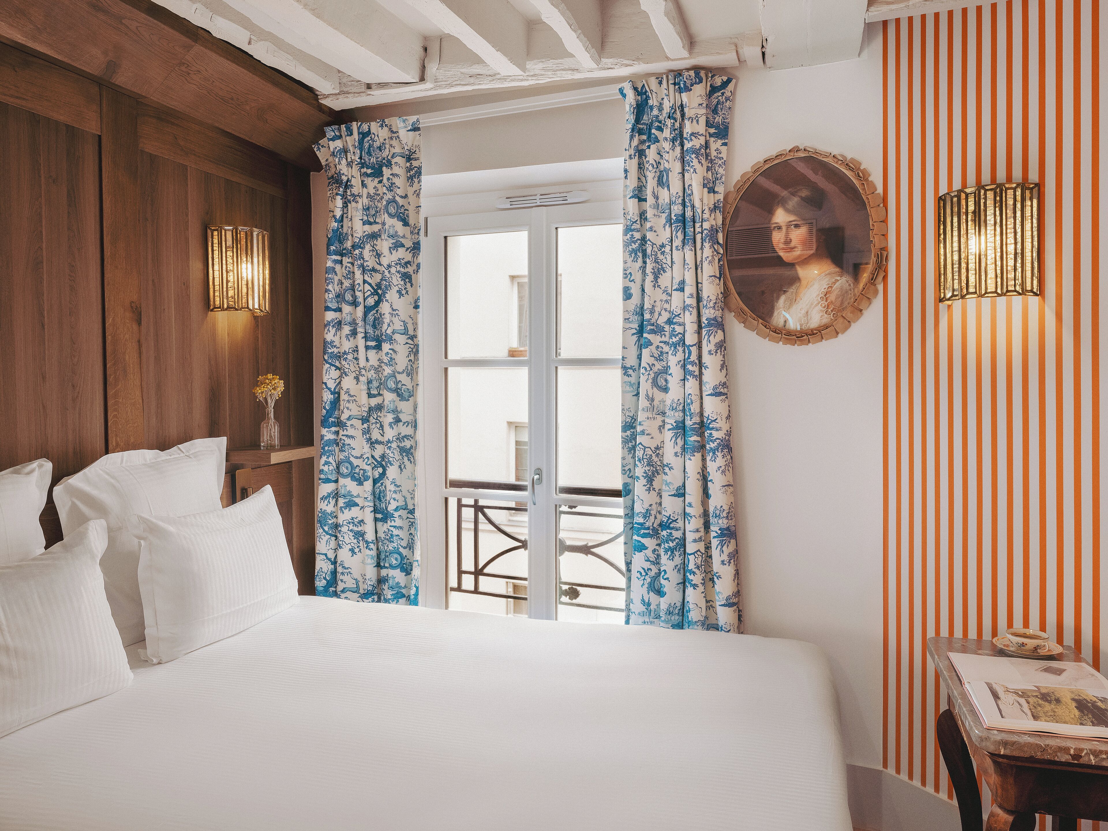 A bedroom with a bed, curtains, a mirror, and a table with a picture frame.