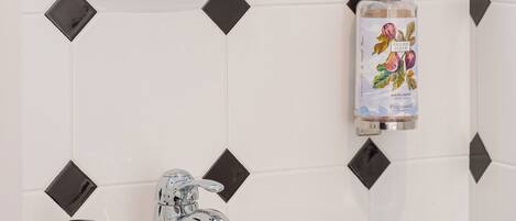Un baño con un lavamanos blanco, un grifo cromado, un espejo redondo y un dispensador de jabón con diseño floral.