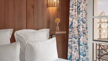 Ein Hotelzimmer mit einer Holzwand, einem Fenster mit blau-blumigen Vorhängen und einem Bett mit weißen Leinen.