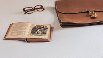 Un libro abierto, gafas y un bolso de cuero marrón cerrado sobre una superficie blanca.