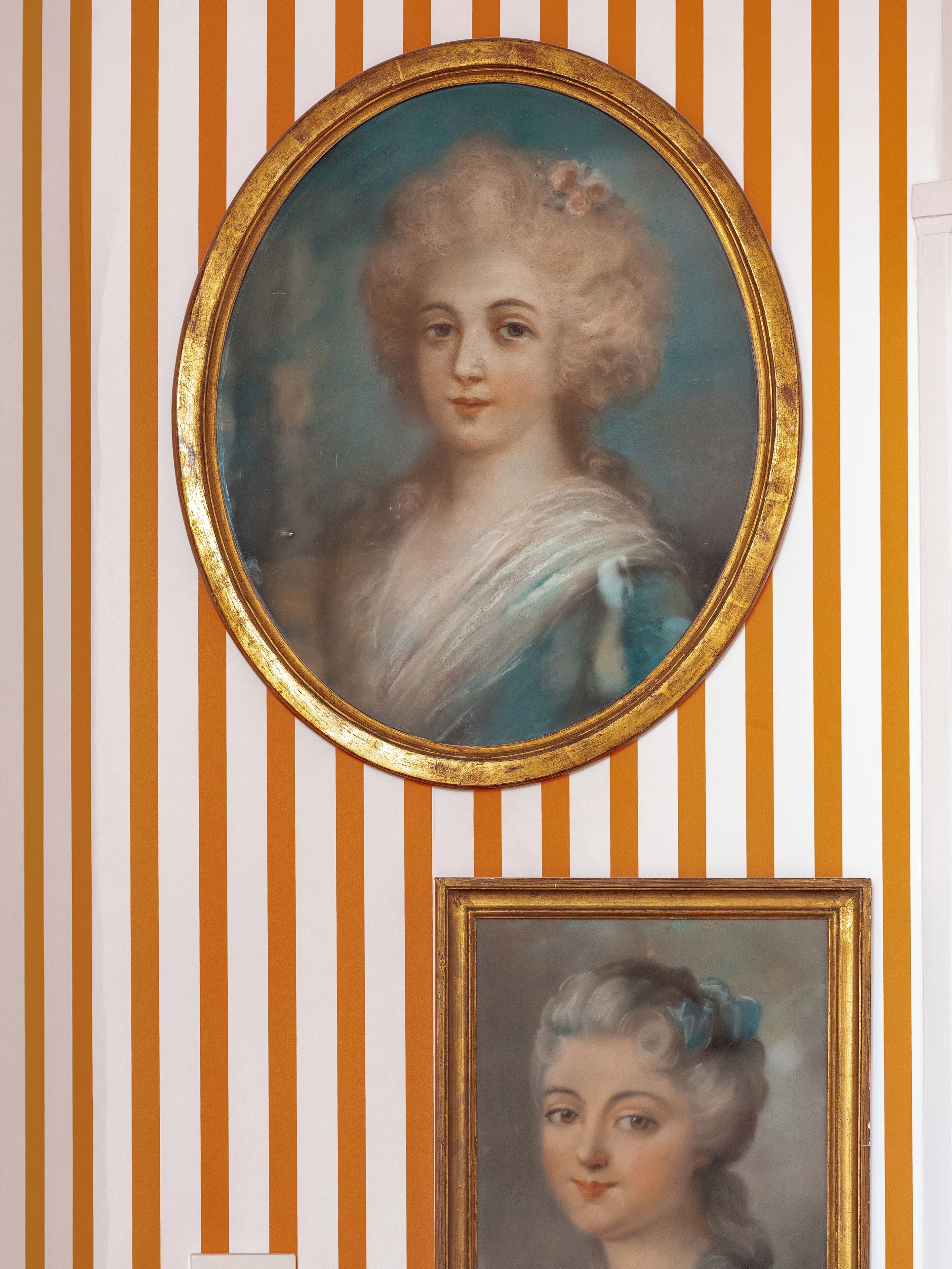 Un portrait encadré d’or, sur un mur à rayures.