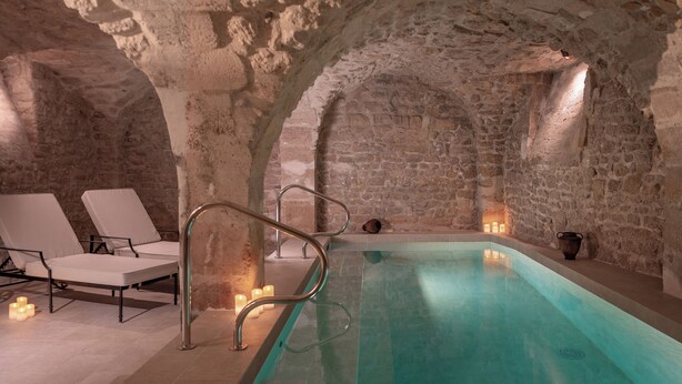 A stone-walled indoor pool with a clear water surface, lounge chairs, and candles. - Hotel Madeleine de Senlis (Paris)