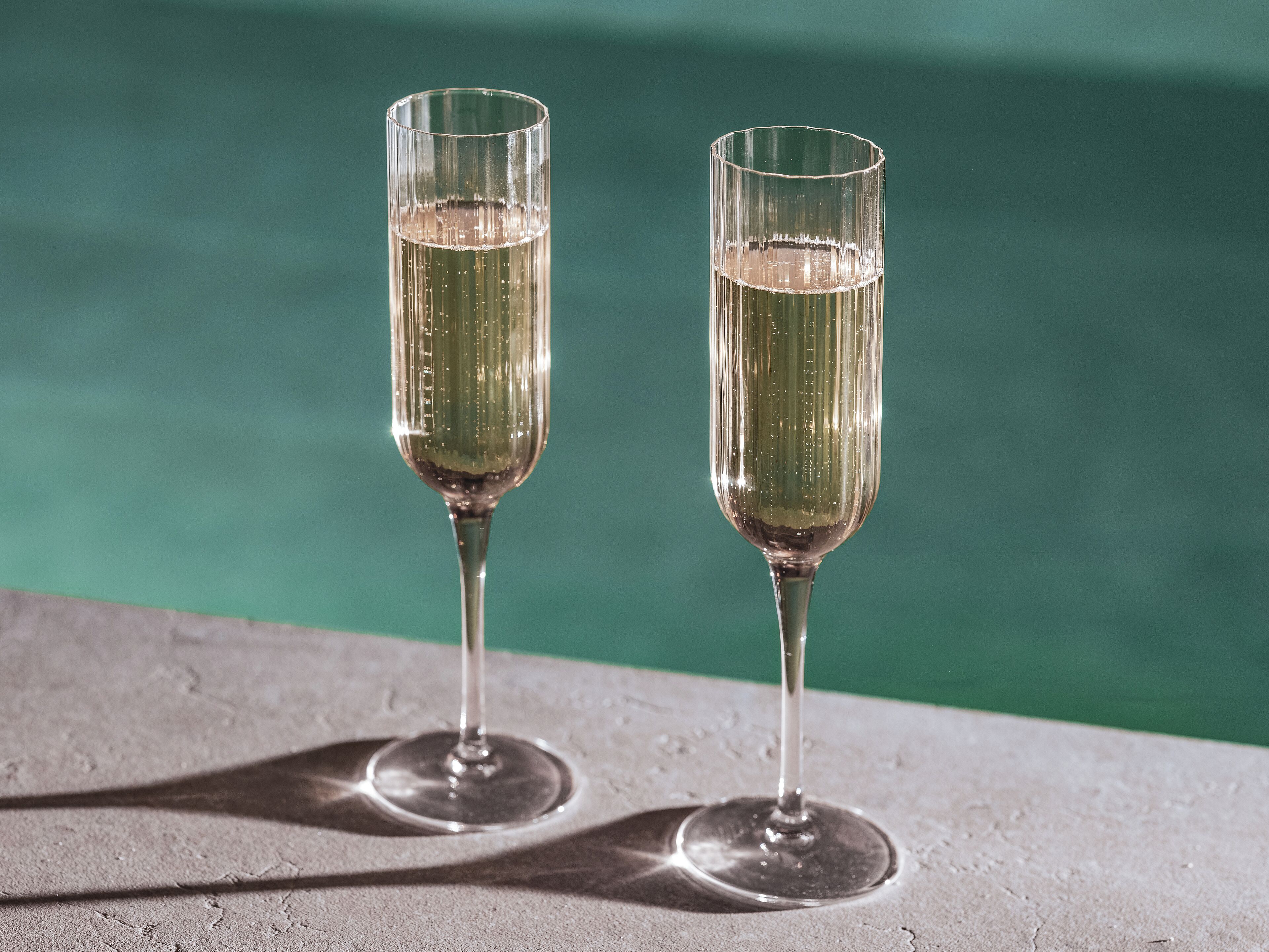 Twee champagneglazen op een betonvloer, met een zwembad op de achtergrond.