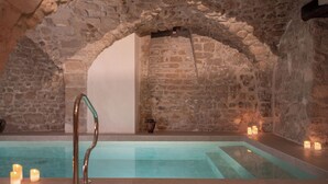 A stone-walled indoor pool with a metal ladder, candles, and a stone bench. - Hotel Madeleine de Senlis (Paris)
