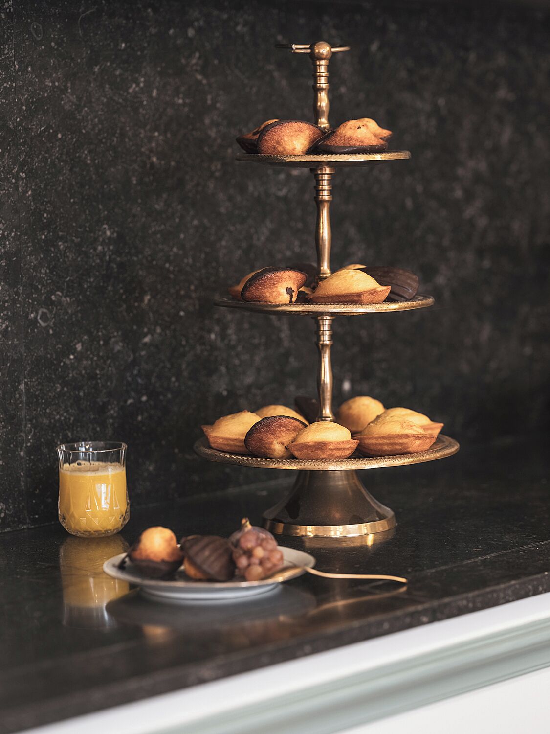 A three-tiered cake stand with cupcakes on a dark countertop.