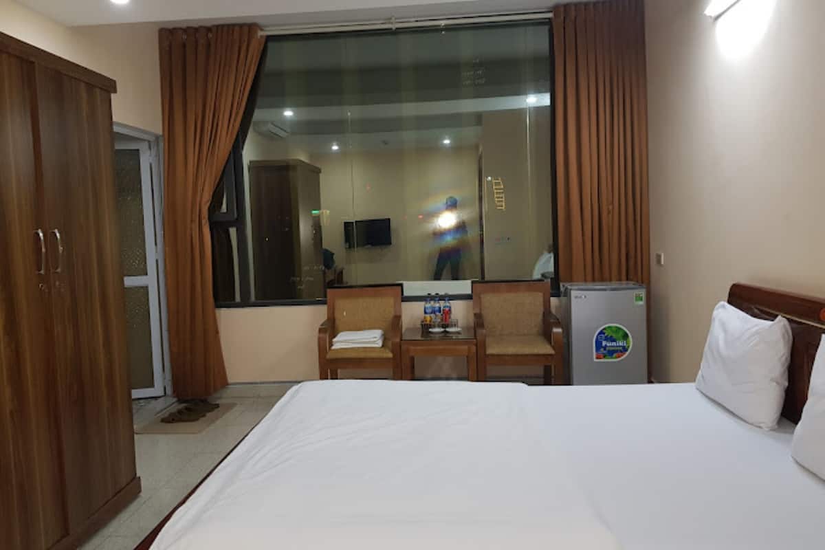 A hotel room with a bed, a desk, a chair, a refrigerator, and a wardrobe.