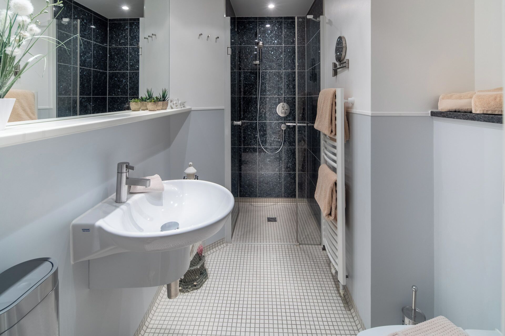 Une salle de bain moderne avec un lavabo blanc, une douche en verre et un sol carrelé.