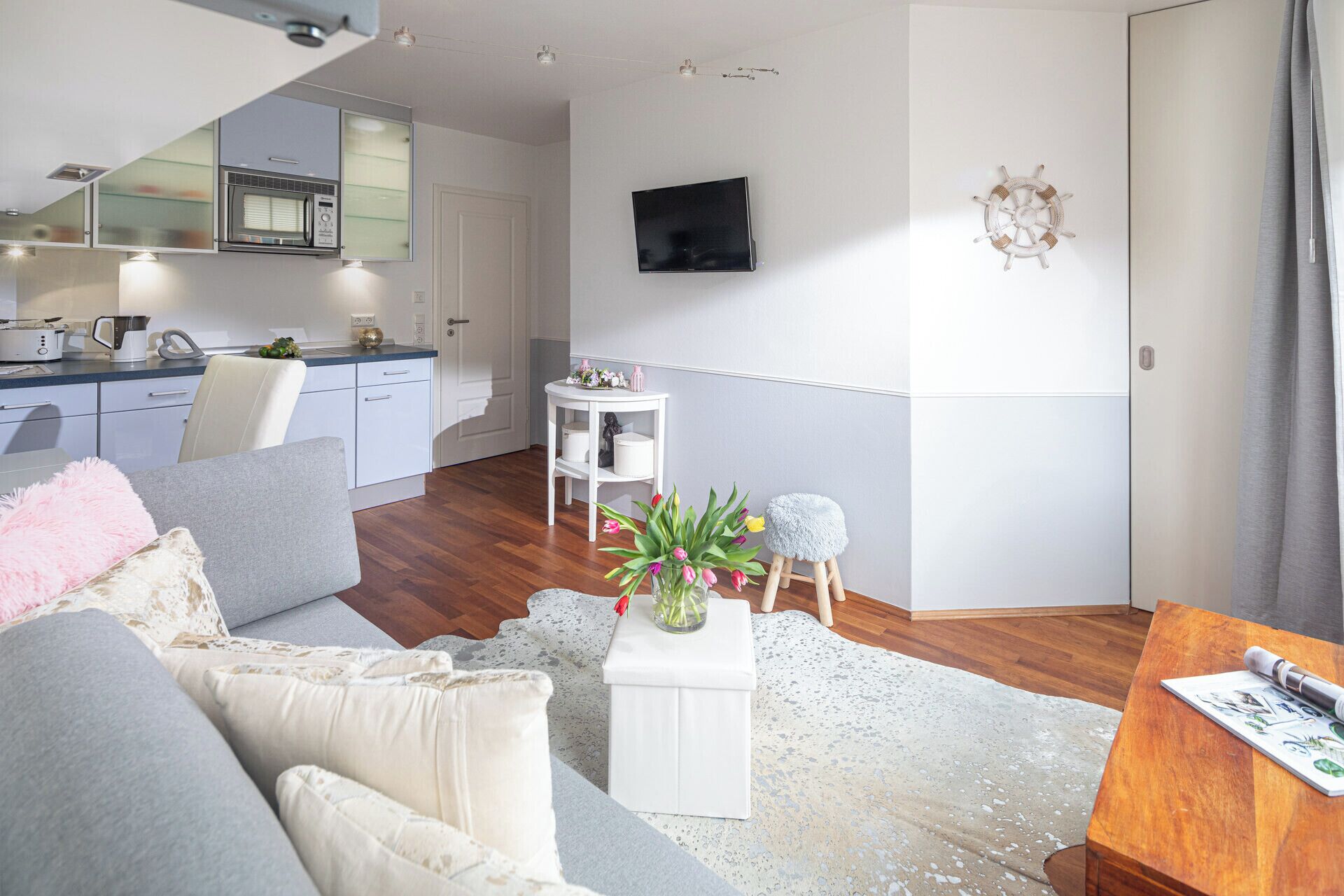 A modern living room with a grey sofa, a white coffee table with a plant, and a wooden dining table.