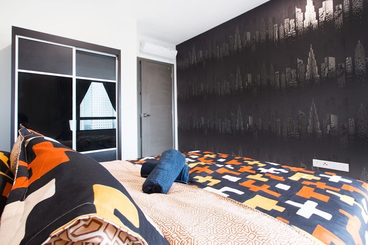 Une chambre à coucher avec un lit, une couverture à motifs et une fresque représentant un paysage urbain sur le mur.