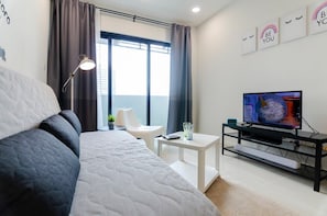 Ein modernes Hotelzimmer mit einem großen Bett, einem kleinen Tisch, einem Fernseher und einem Balkon mit Vorhängen.