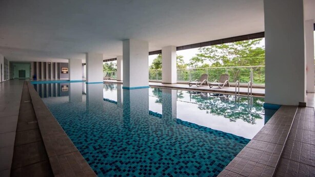 Una piscina interior con agua azul cristalina, rodeada de pilares blancos y un suelo de baldosas.
