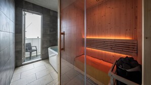 A modern bathroom with a glass shower enclosure, a wooden sauna area, and a seating area with a chair. - Kanatanosato (Wakayama)