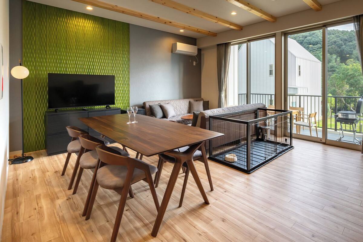 A modern living room with a wooden dining table, sofa, and a pet cage.
