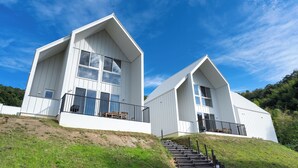 Two white, modern houses with large windows and balconies, situated on a grassy hill with a clear sky. - Kanatanosato (Wakayama)