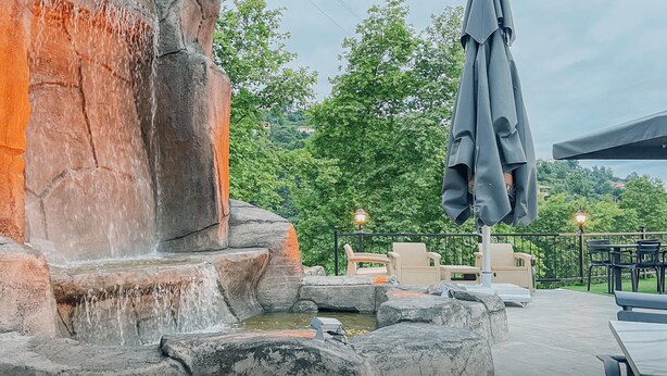 A stone water feature with cascading water, surrounded by outdoor seating and a view of greenery. - Kastel Konak Hotel (Surmene)