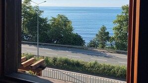 A view through a window of a road with a guardrail, trees, and a clear blue sky. - Kastel Konak Hotel (Surmene)