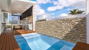 Un área de piscina exterior moderna con un muro de piedra y una terraza de madera.