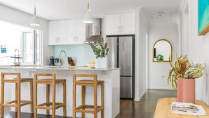 Una cocina moderna con armarios blancos, un refrigerador de acero inoxidable y una barra con taburetes de madera.