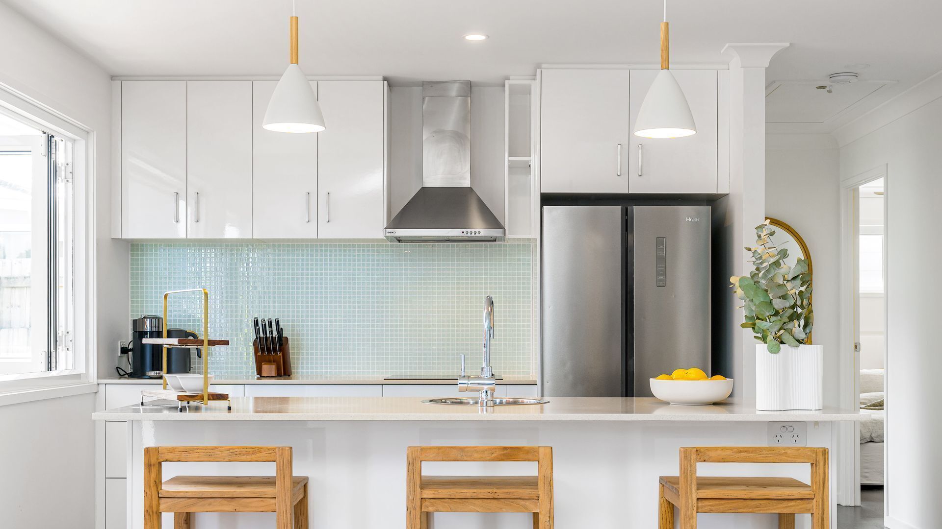 A modern kitchen with white cabinetry, stainless steel appliances, and wooden bar stools.