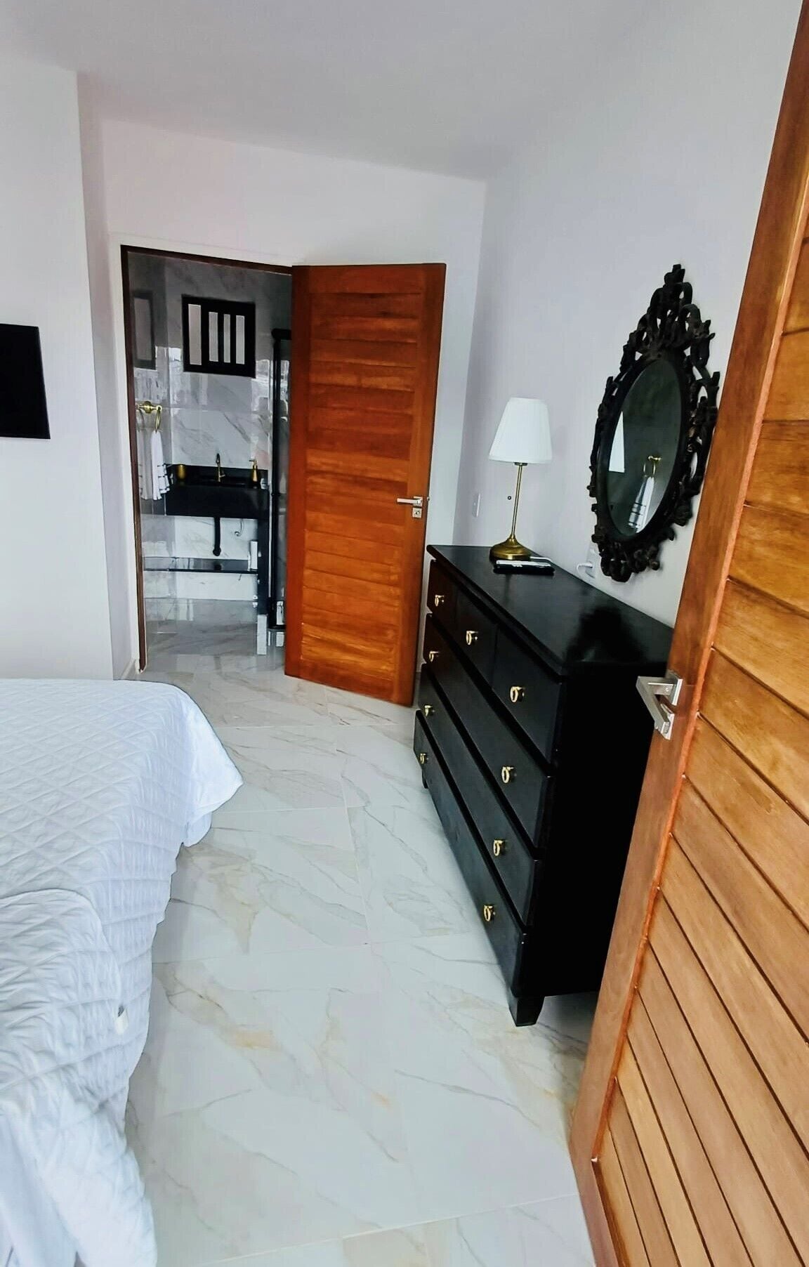 Una camera da letto con un letto, una cassettiera, uno specchio e un bagno parzialmente visibile attraverso una porta aperta.